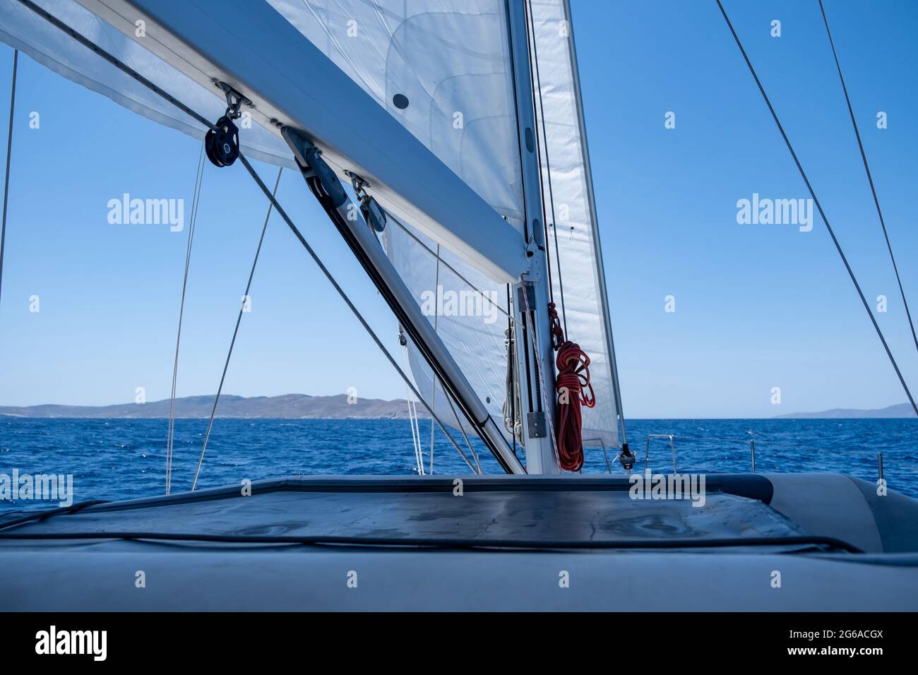 Yacht a vela in pendenza bianca in un oceano aperto e tranquillo, cielo blu sullo sfondo, giorno di sole. Vista in primo piano della barca a vela, prua, albero e vele. Marinai del mar Egeo Foto Stock