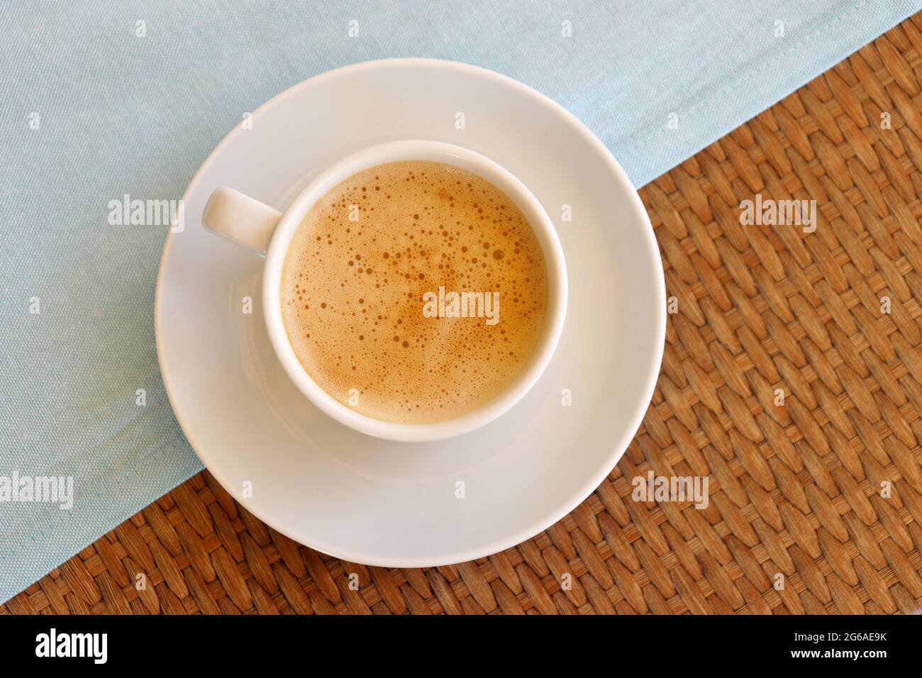 Tazza di cappuccino in un piattino bianco su tavolo di legno con tovaglia, vista dall'alto Foto Stock