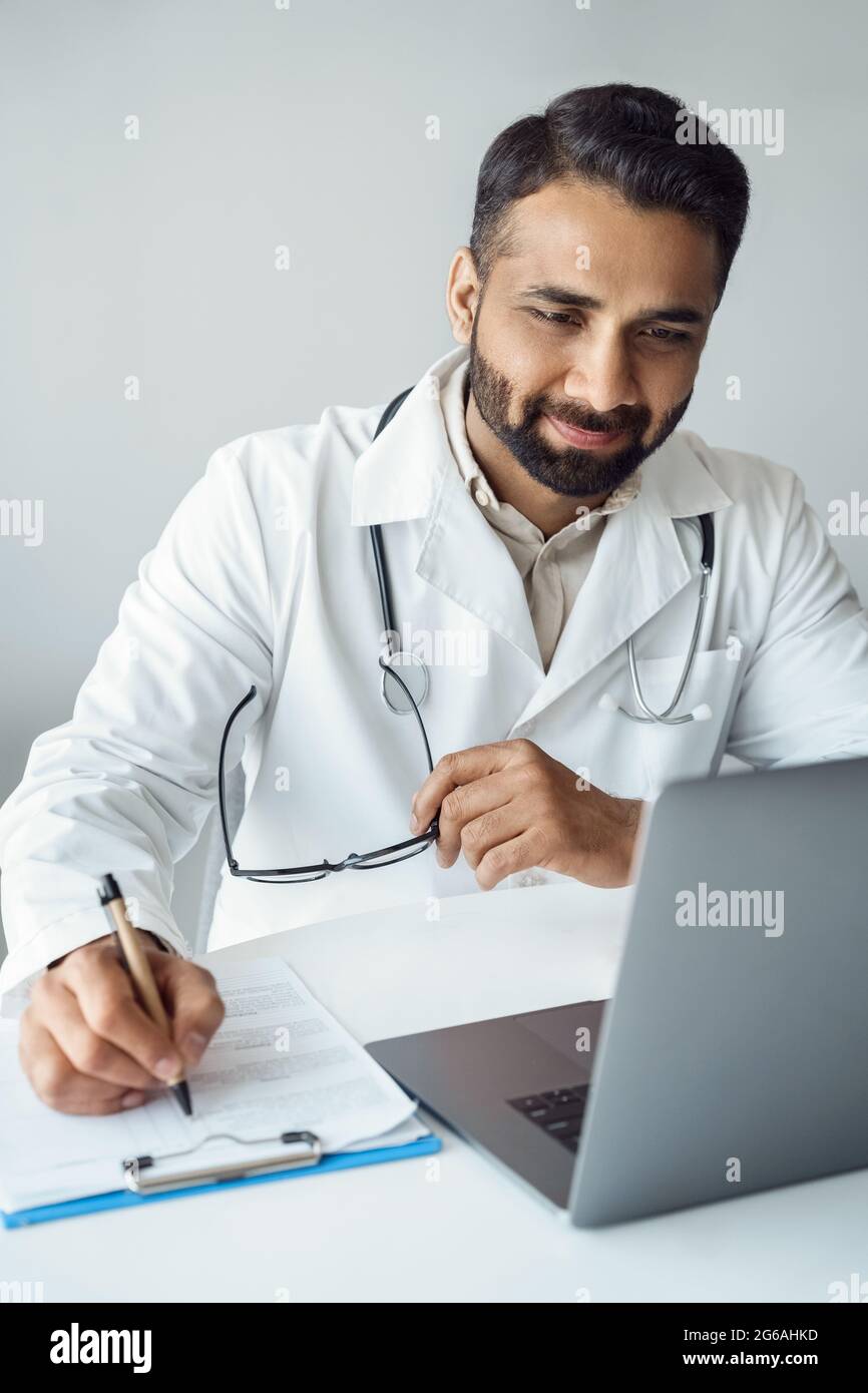 Medico maschile indiano che guarda lo schermo del computer portatile durante la consultazione online Foto Stock