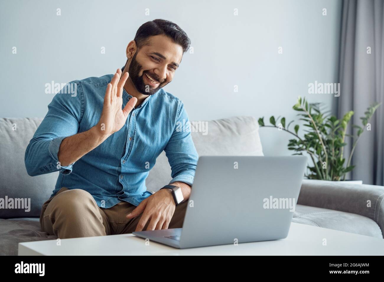 Uomo d'affari indiano che sventola la mano al cliente online utilizzando un computer portatile Foto Stock