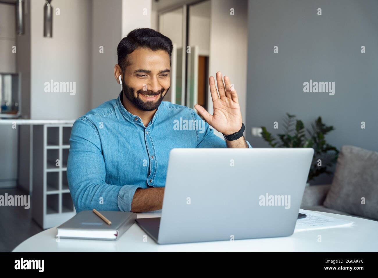 Uomo arabo che svetta la mano con un gesto di saluto che guarda lo schermo del laptop Foto Stock