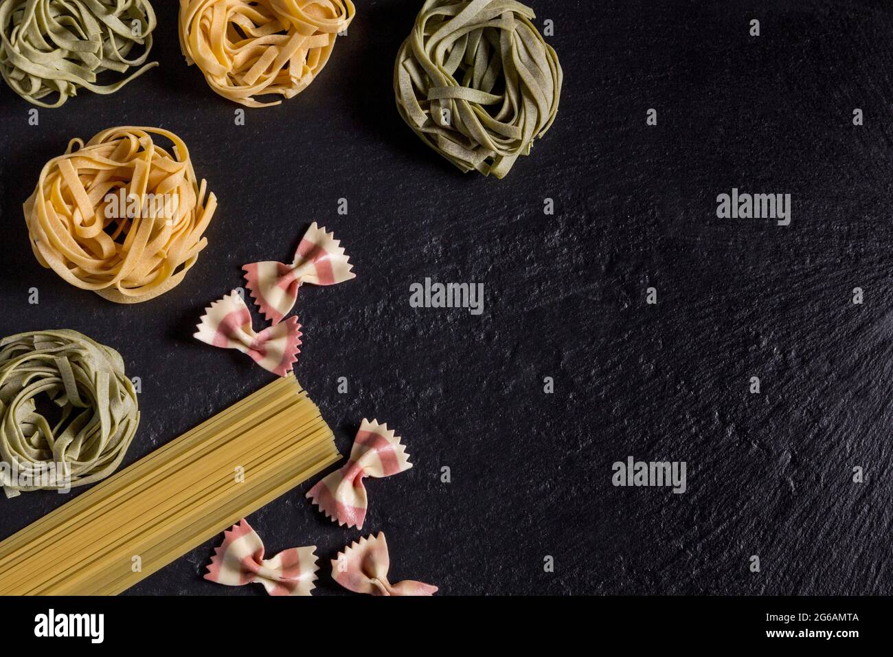 Tagliatelle verdi e gialle, spaghetti e farfalle di pasta su ardesia nera Foto Stock