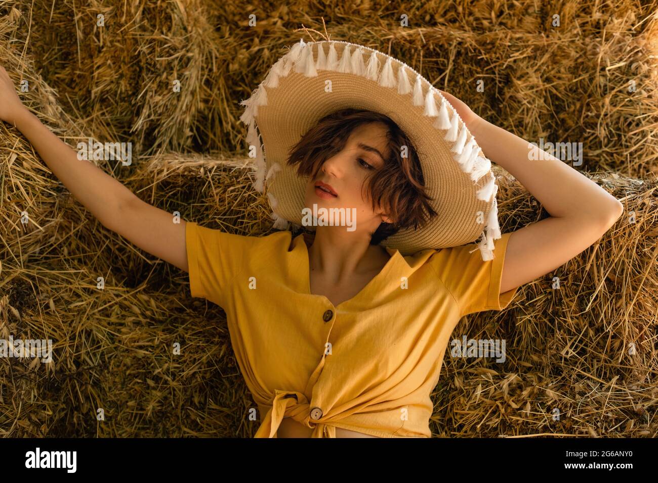 Ritratto di una donna con un cappello di paglia, camicia gialla seduta in un fienile. Foto Stock