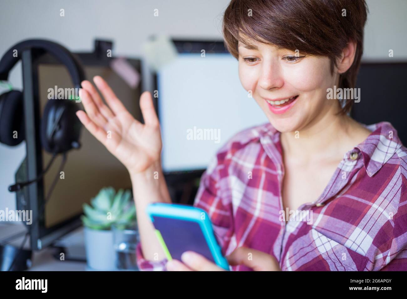 Donna felice, emozionale, sorridente guardando il suo smartphone, sentire gioiosa leggere buone notizie, fare gesti e leggere le buone notizie mentre si siede a. Foto Stock