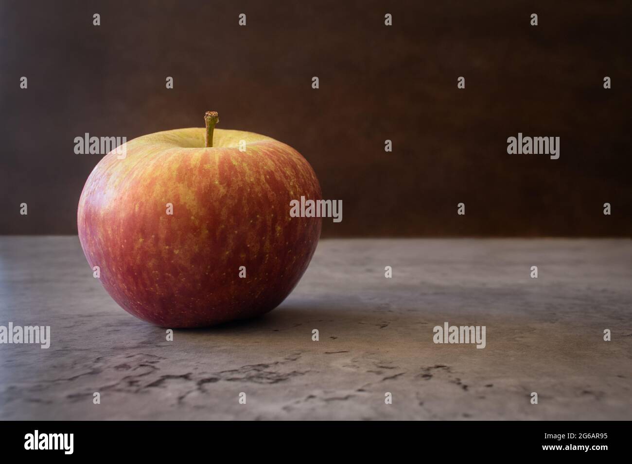 Vita morta di una mela fuji con allineamento a sinistra poggiato su un contatore isolato su uno sfondo scuro a trama. Fotografia di frutta con spazio per il testo Foto Stock