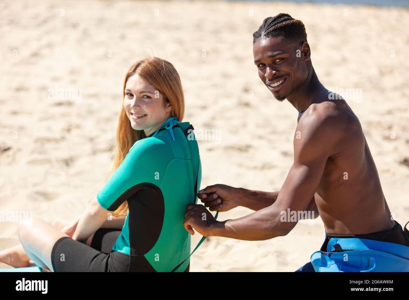 giovane uomo che chiude la tuta da surf womans sulla spiaggia Foto Stock