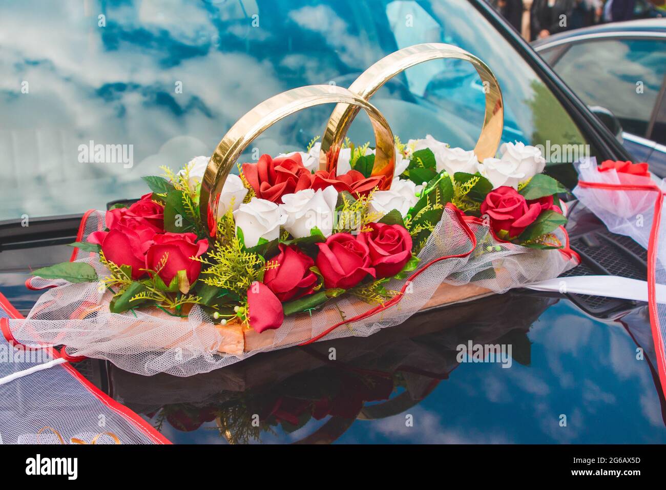 Decorazione nuziale della macchina sotto forma di anelli, colori artificiali di rose rosse e bianche sul cofano della macchina. Foto Stock
