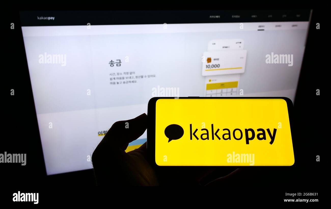 Persona che tiene il cellulare con il logo della società di pagamento sudcoreana KakaoPay Corp. Sullo schermo davanti alla pagina web di affari. Mettere a fuoco il display del telefono. Foto Stock