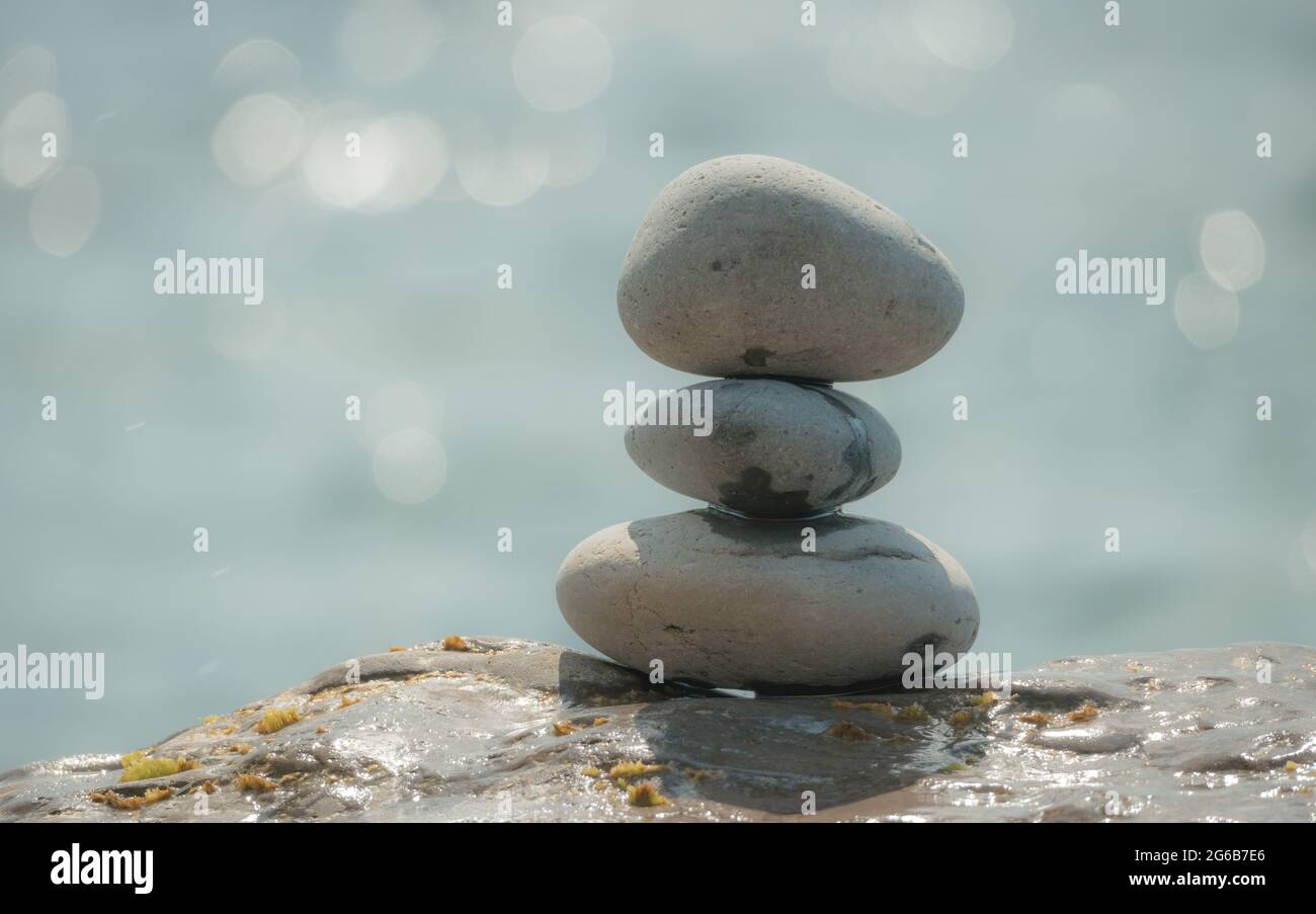 Equilibrata piramide di ciottoli sulla spiaggia in una giornata di sole. Abstract Sea bokeh sullo sfondo. Messa a fuoco selettiva. Pietre Zen sulla spiaggia di mare, meditazione Foto Stock