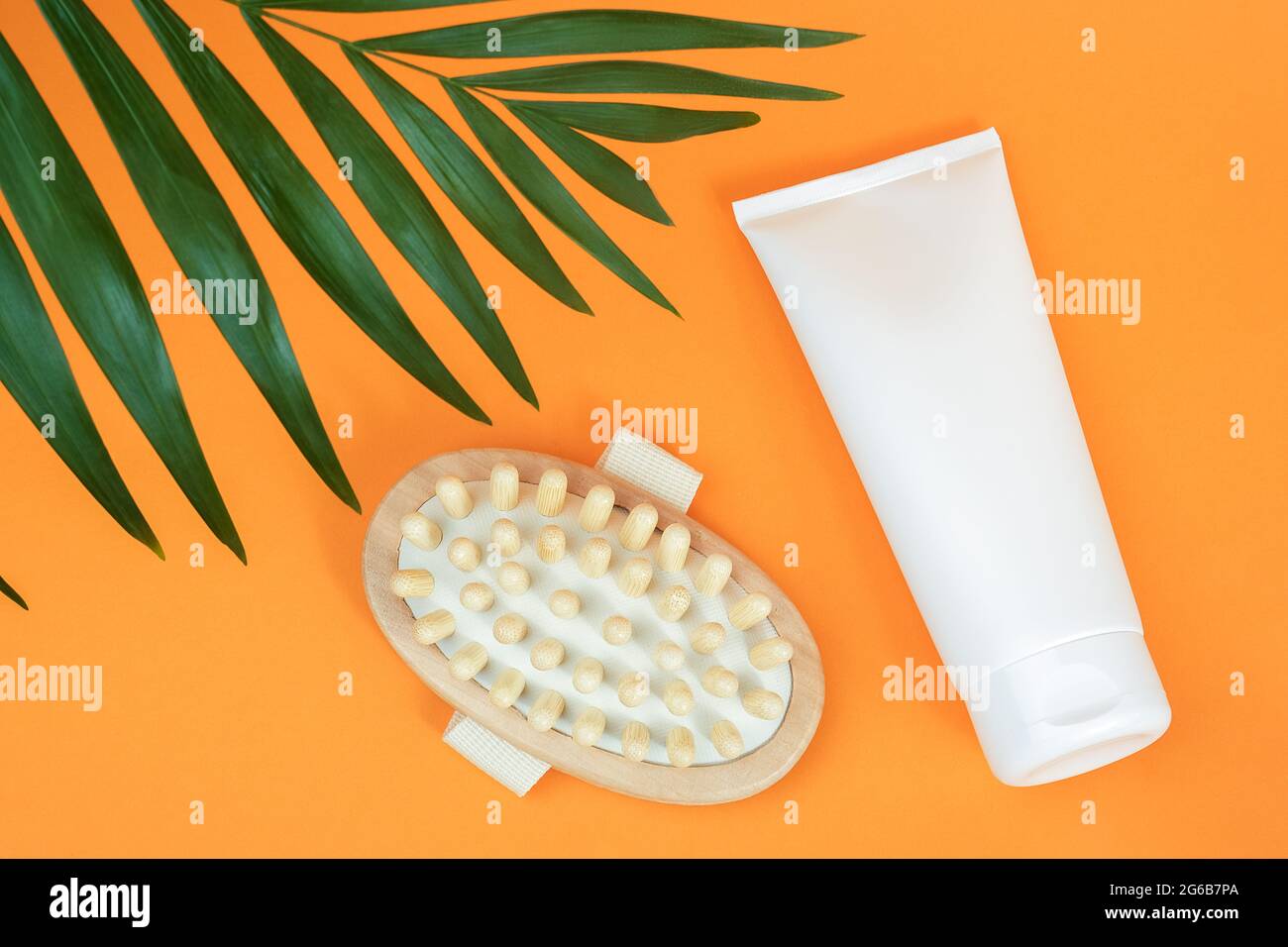 Tubo cosmetico bianco di crema o lozione per il corpo e massaggiatore anticellulite in legno, foglia di palma su sfondo arancione. Lotta concettuale contro la cellulite. Foto Stock