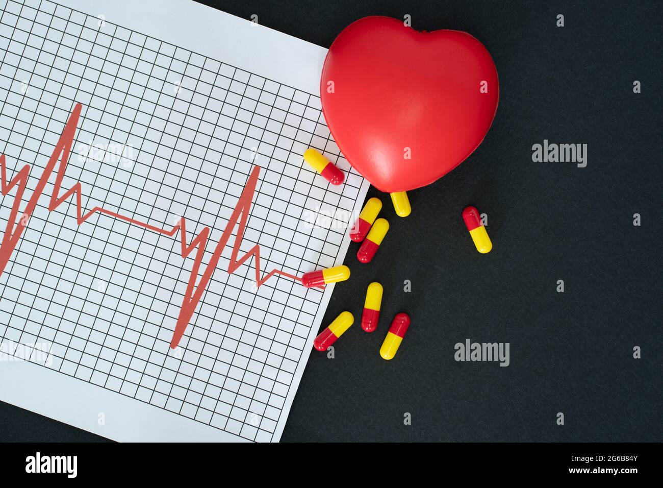 Layout di un elettrocardiogramma, alcune pillole e un modello a forma di cuore su sfondo nero Foto Stock