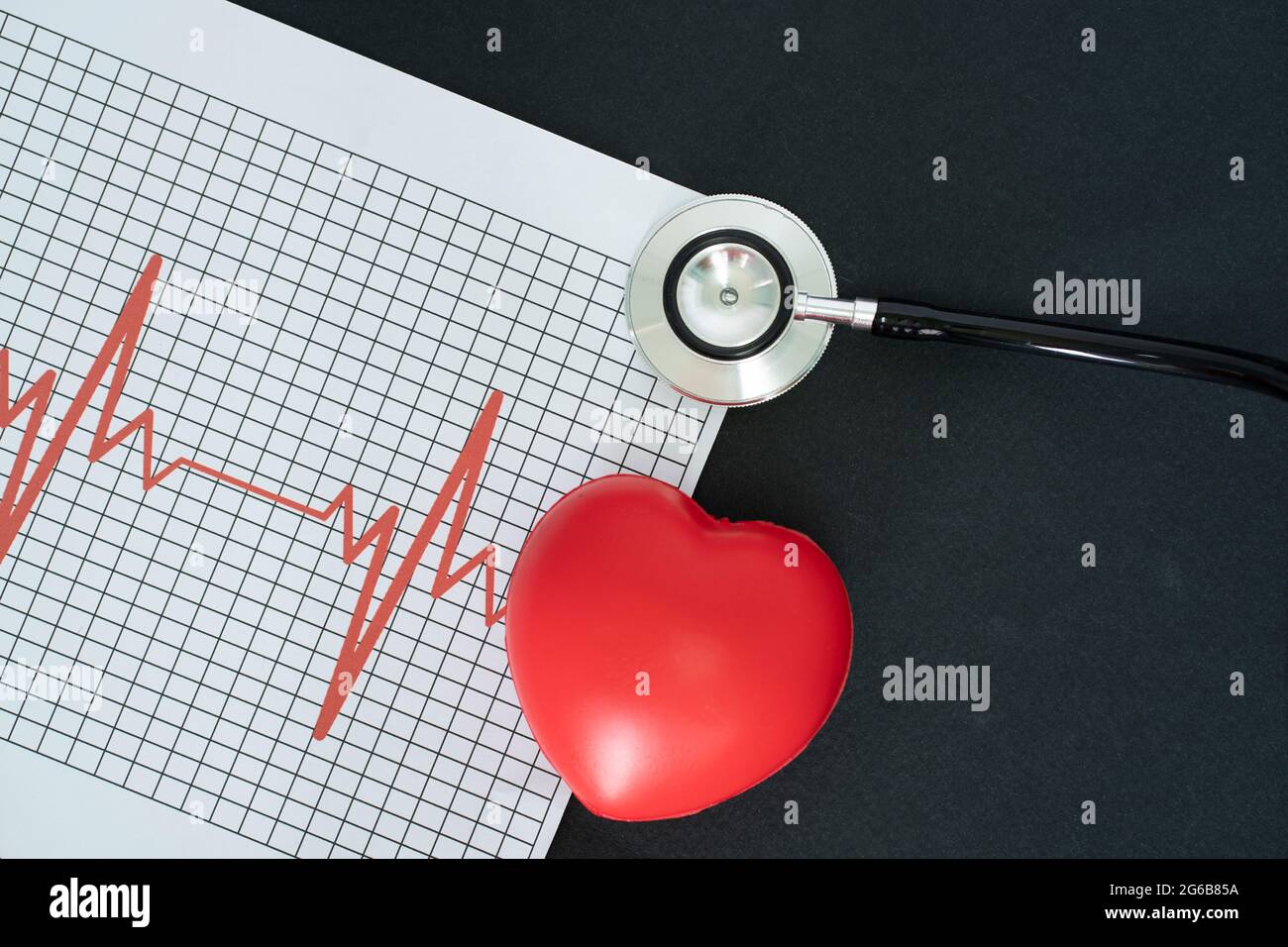 Layout di un elettrocardiogramma, di uno stetoscopio e di un modello a forma di cuore su sfondo nero Foto Stock