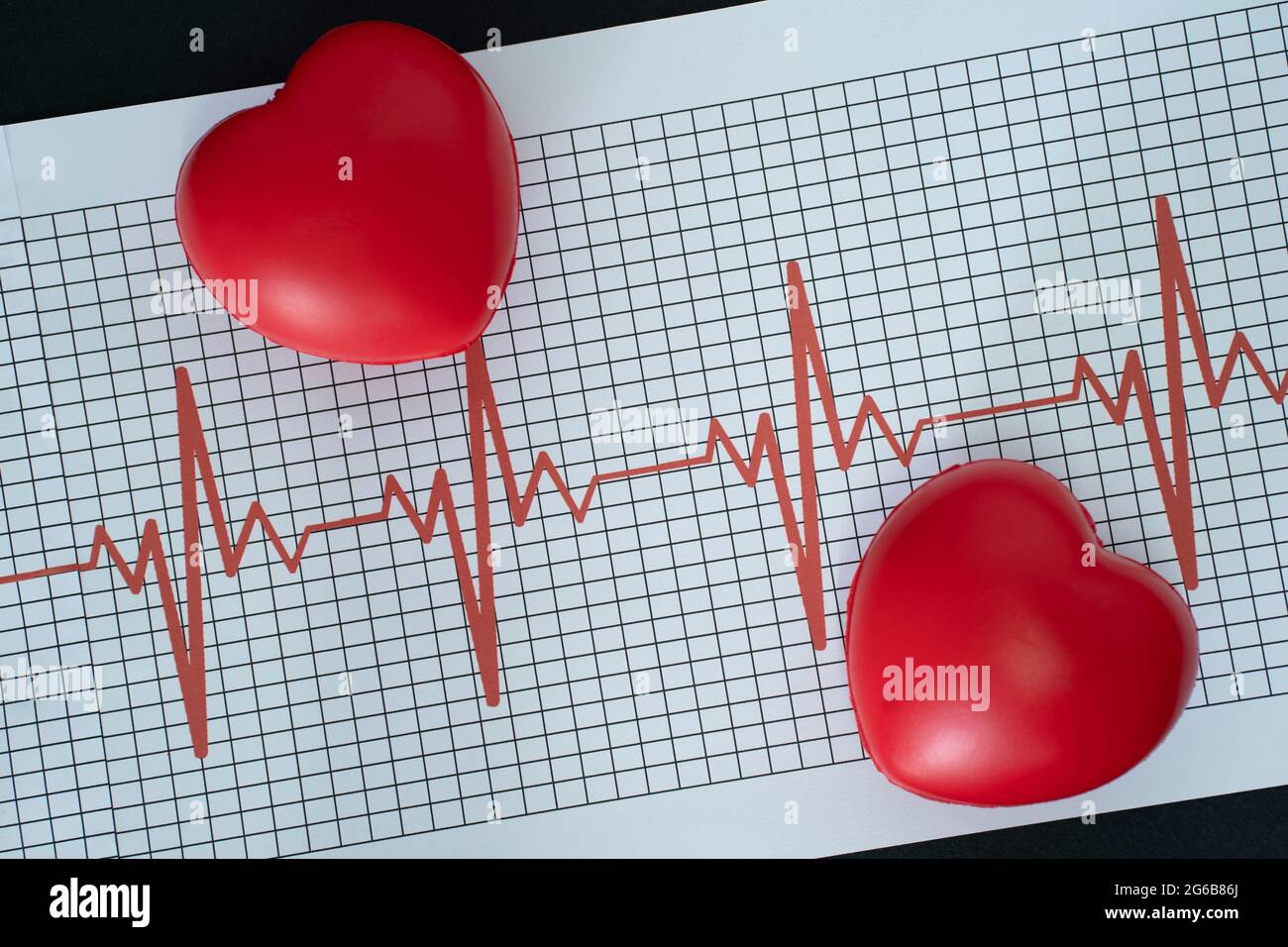 Layout di un elettrocardiogramma e di due modelli a forma di cuore su sfondo nero Foto Stock