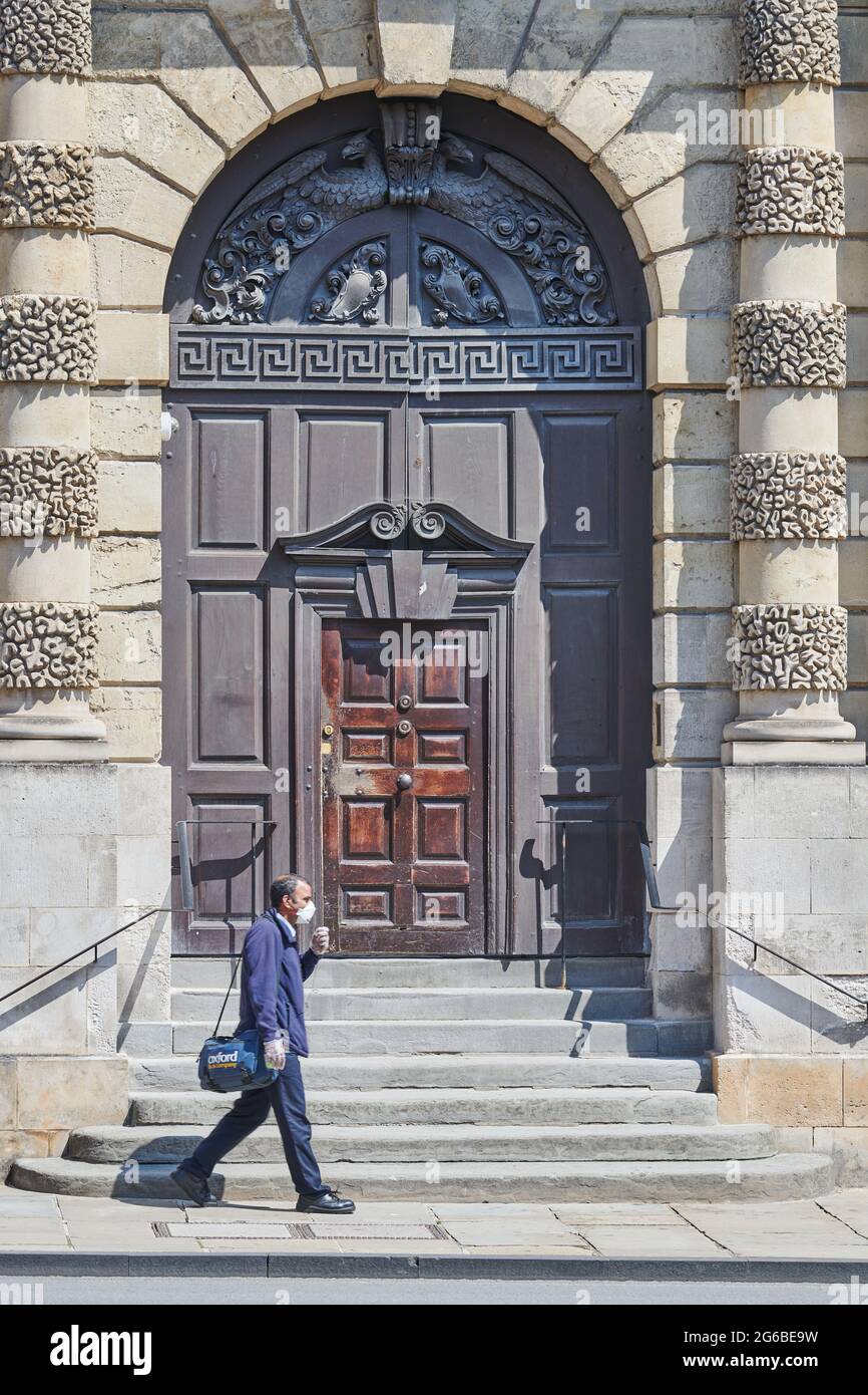 Un uomo che indossa una maschera passa davanti al Queen's College, università di Oxford, Inghilterra, giugno 2021. Foto Stock