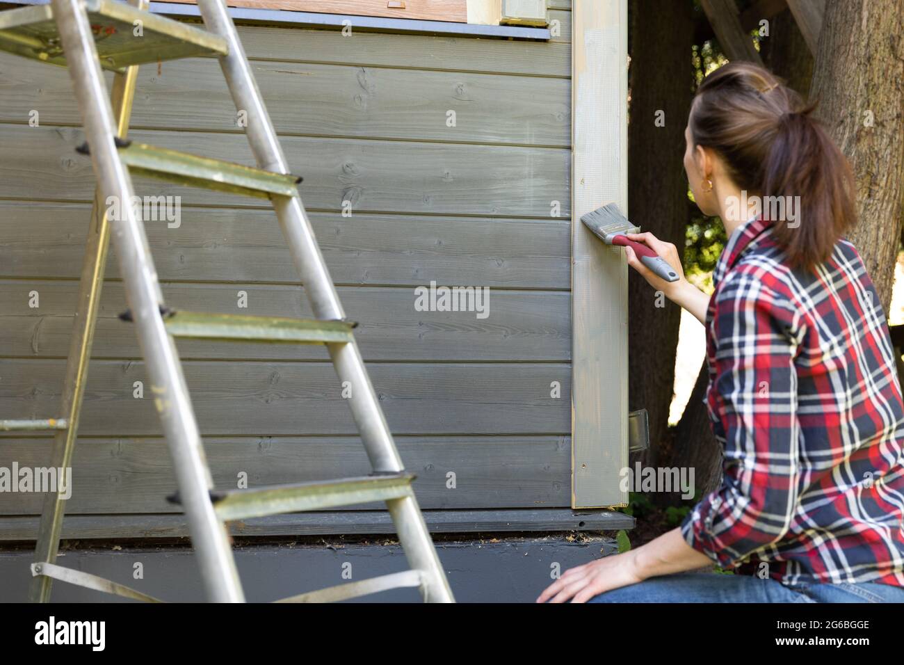 Donna lavoratore pittura legno casa parete esterna con pennello e legno protettivo colore casa miglioramento concetto. Foto Stock