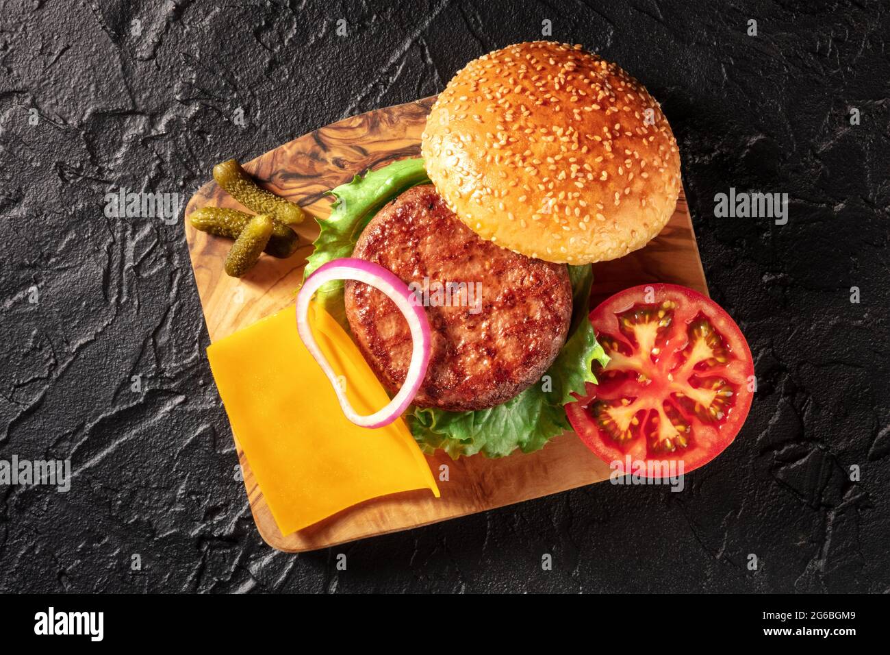 Ingredienti Burger, sparati dall'alto su uno sfondo nero. Hamburger di carne di manzo, formaggio Cheddar, verdure, panini al sesamo e sottaceti Foto Stock