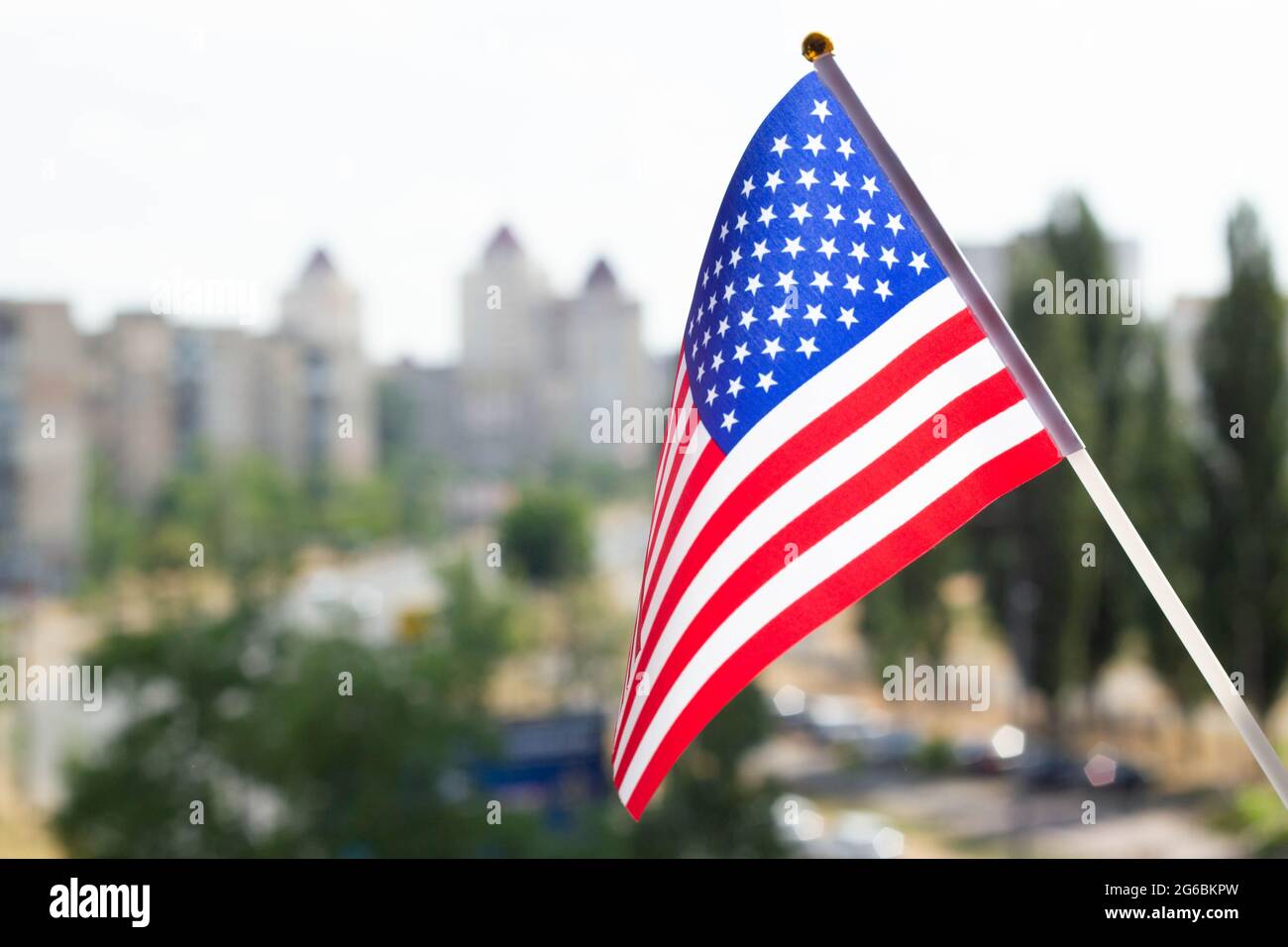 Bandiera degli Stati Uniti d'America contro il cielo blu, gli alberi verdi, la strada della città e gli edifici a più piani. Visualizzazione della bandiera US su una finestra della casa Foto Stock