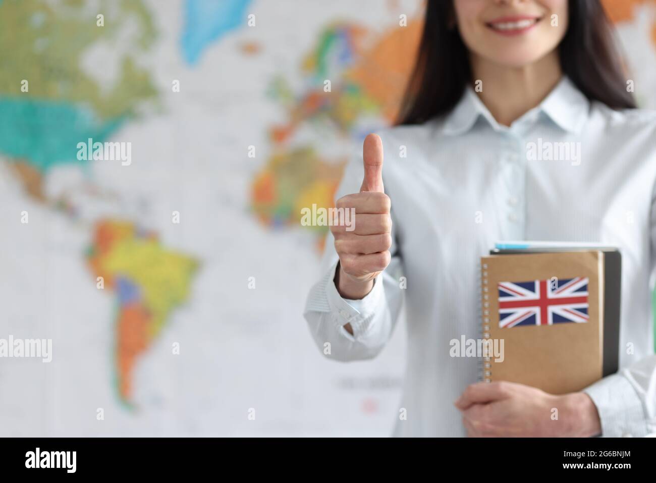 Donna che tiene libri di testo in inglese sullo sfondo della mappa del mondo e che mostra il pollice in su primo piano Foto Stock