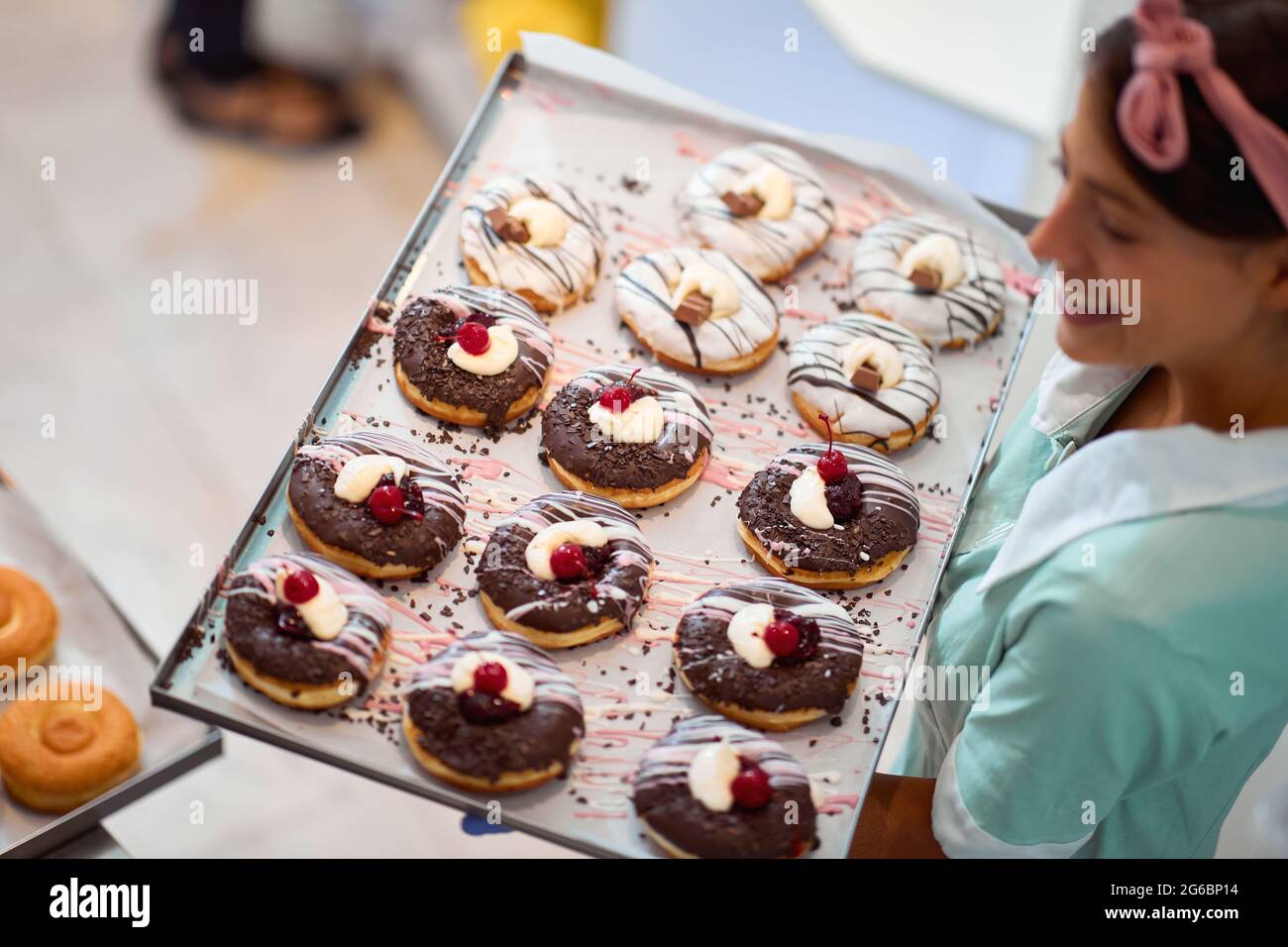 Una giovane piccola impresa donna proprietario è tenere un vassoio di deliziose ciambelle fatte a mano di irresistibilità aspetto fatto con amore pronto per una pasta sho Foto Stock
