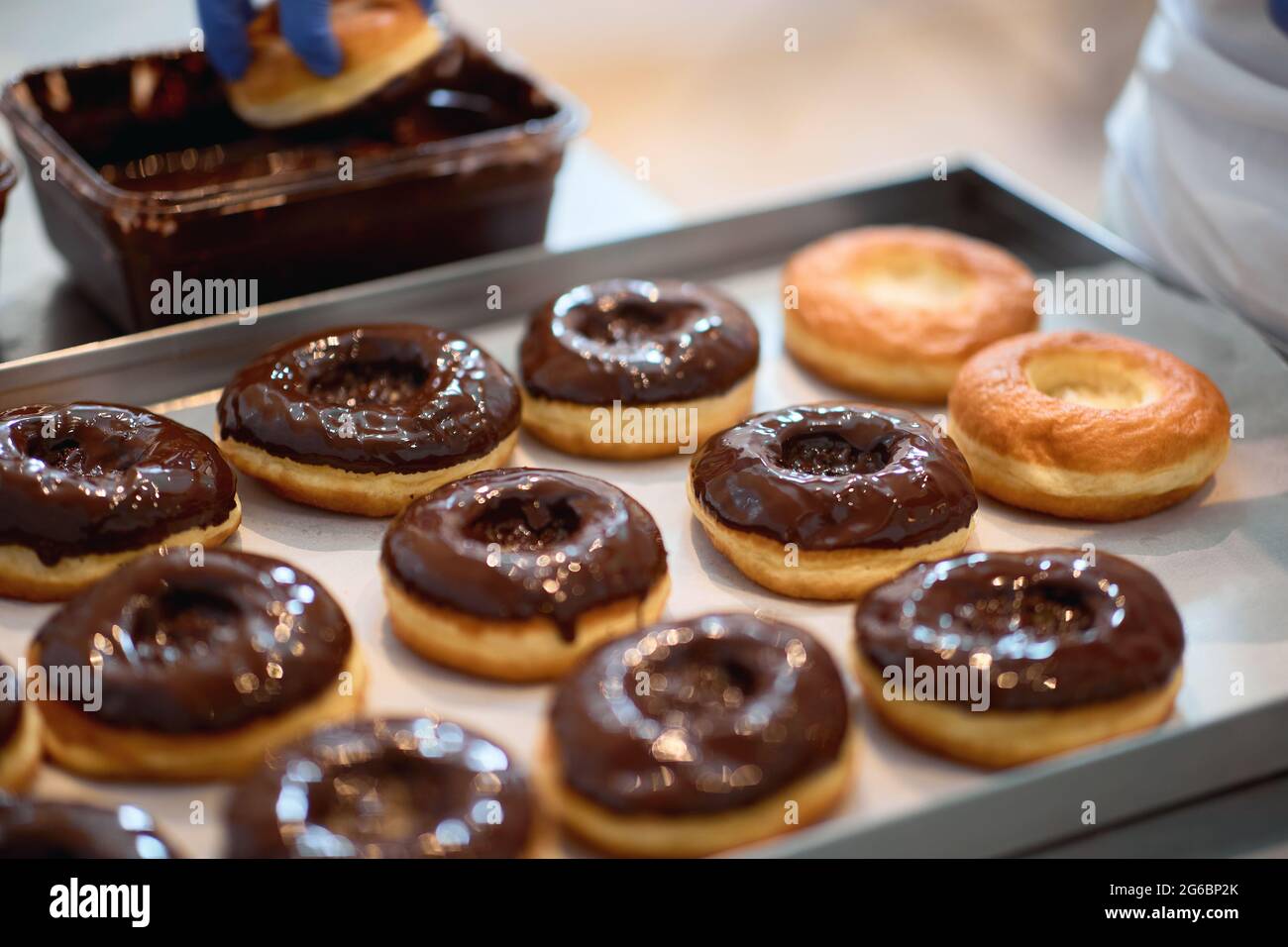 Un operaio sta facendo la copertura delle ciambelle con la guarnizione del cioccolato in un'atmosfera di lavoro in un laboratorio della caramella. Pasticceria, dessert, dolce, fare Foto Stock