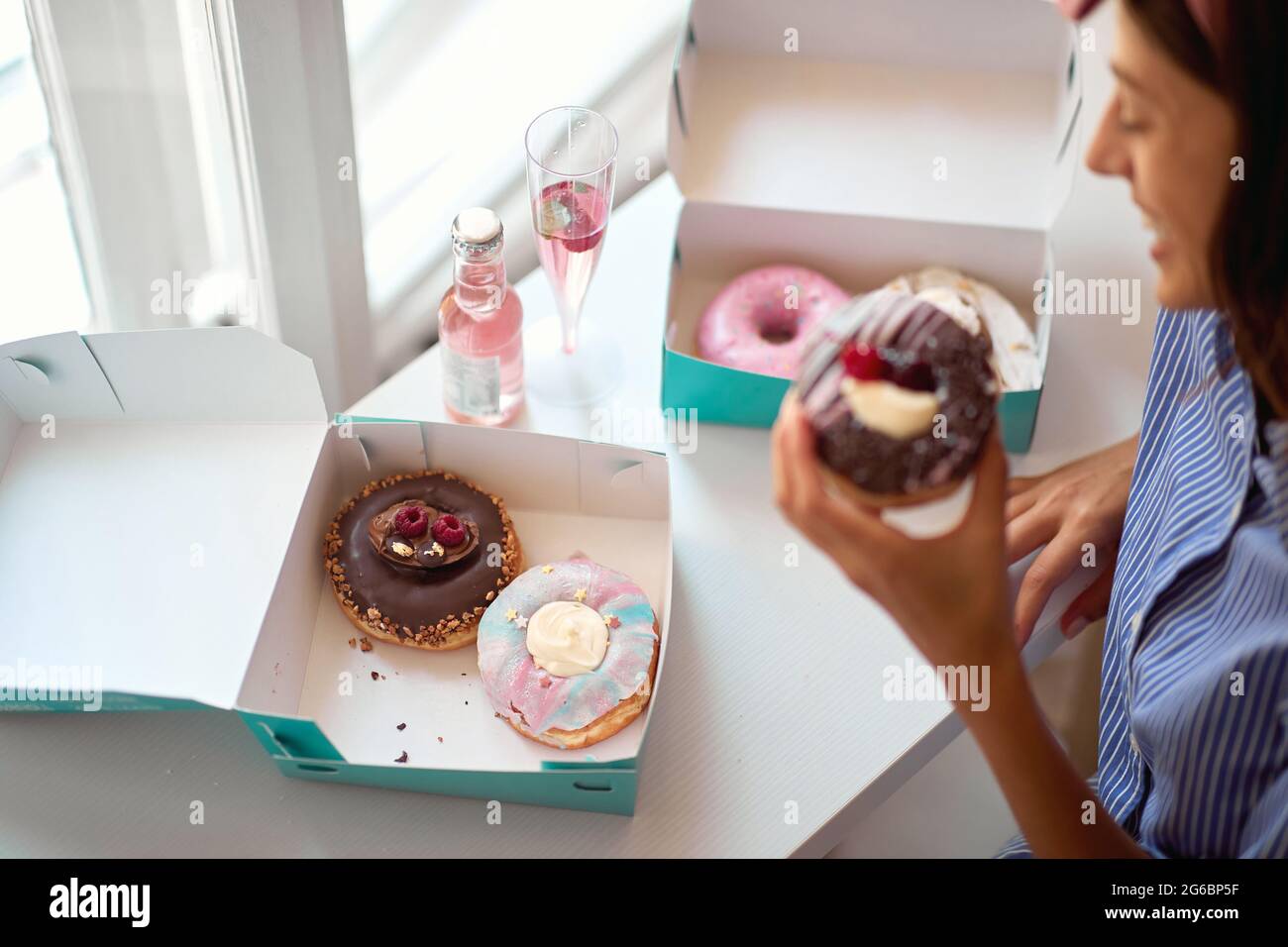 Donna allegra che mangia deliziose ciambelle a casa Foto Stock