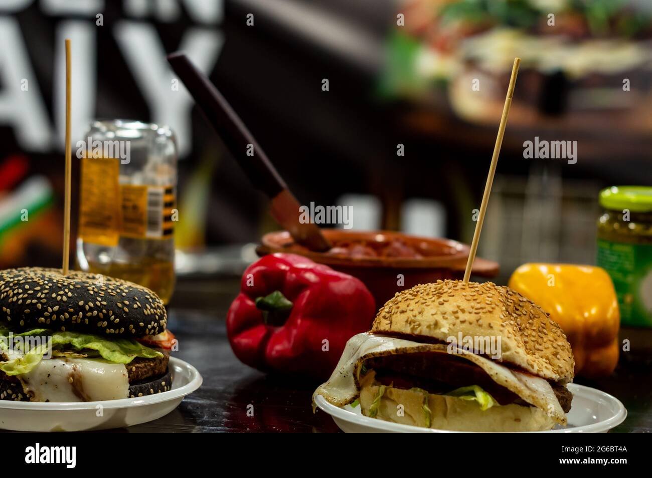Due hamburger di formaggio su un tavolo con peperoni rossi e gialli sullo sfondo del bancone del cibo di strada Foto Stock