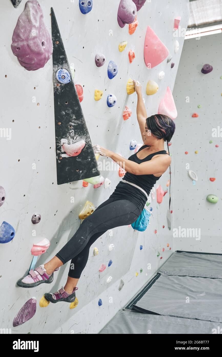 Adatta una giovane donna forte che salta su una parete di bouldering senza dispositivi auto belay Foto Stock