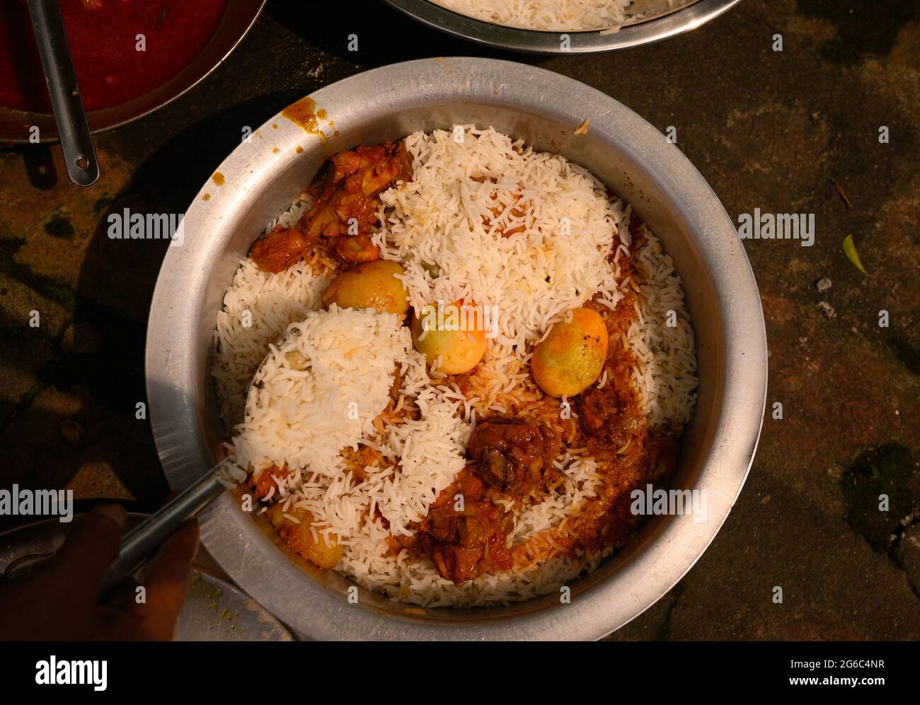 Una donna sta cucinando biryani. Biryani è una parola indo-ariana derivata dalla parola persiana 'Birian', che significa ‘fritto prima di cucinare' e 'Birinj', la parola persiana per il riso. Il Biryani è uno dei piatti più popolari e ordinati in India. È fatto con spezie indiane, riso e carne (pollo, manzo, capra, agnello, gamberetto, pesce), e talvolta, in aggiunta, uova o ortaggi, come le patate di alcune varietà regionali. Ci sono varie teorie relative all'origine di questo piatto delizioso. Molti storici credono che i biryani provenivano dalla Persia e sono stati portati in India dai Mughals. Foto Stock