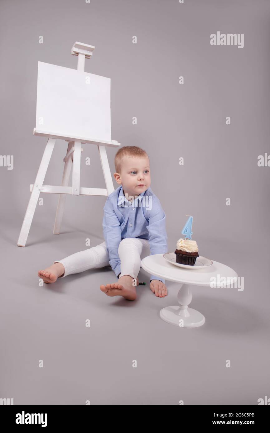 prescolare ragazzo in pantaloni bianchi e camicia blu su sfondo grigio  vicino cavalletto con mockup e cupcake con candela, modellato in numero  quattro 4. buon compleanno Foto stock - Alamy