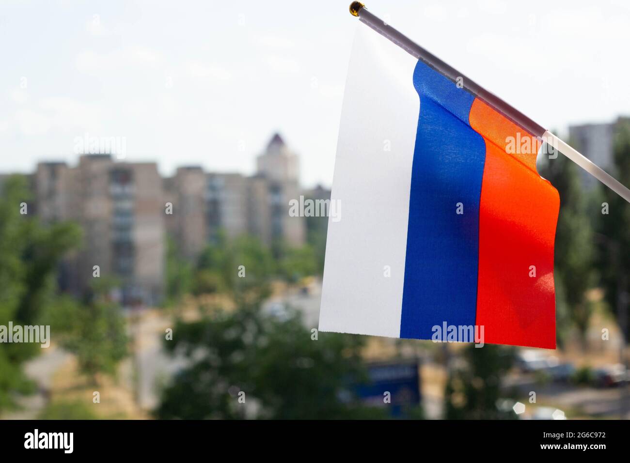 Bandiera della Russia ambientata contro il cielo blu, gli alberi verdi, la strada della città e gli edifici a più piani. La bandiera di vacanza della Federazione Russa Foto Stock