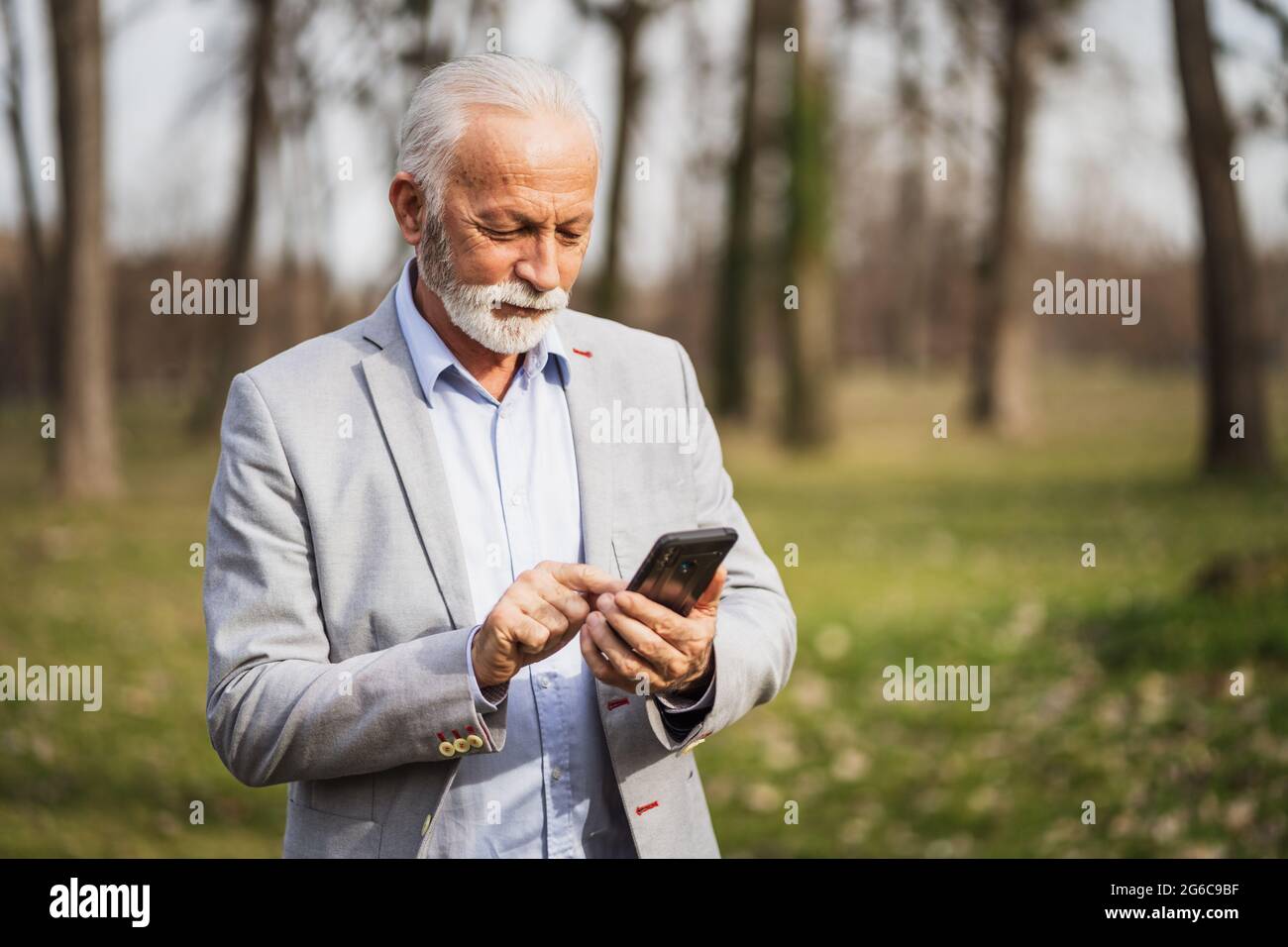 Felice uomo d'affari senior è rilassante dopo il lavoro. Sta utilizzando lo smartphone per la messaggistica. Foto Stock