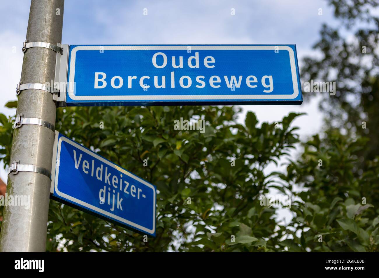 WIERDEN, OLANDA - 10 settembre 2020: Cartello stradale olandese in blu con lettera bianca contro un cielo blu con nuvole e verde sullo sfondo Foto Stock