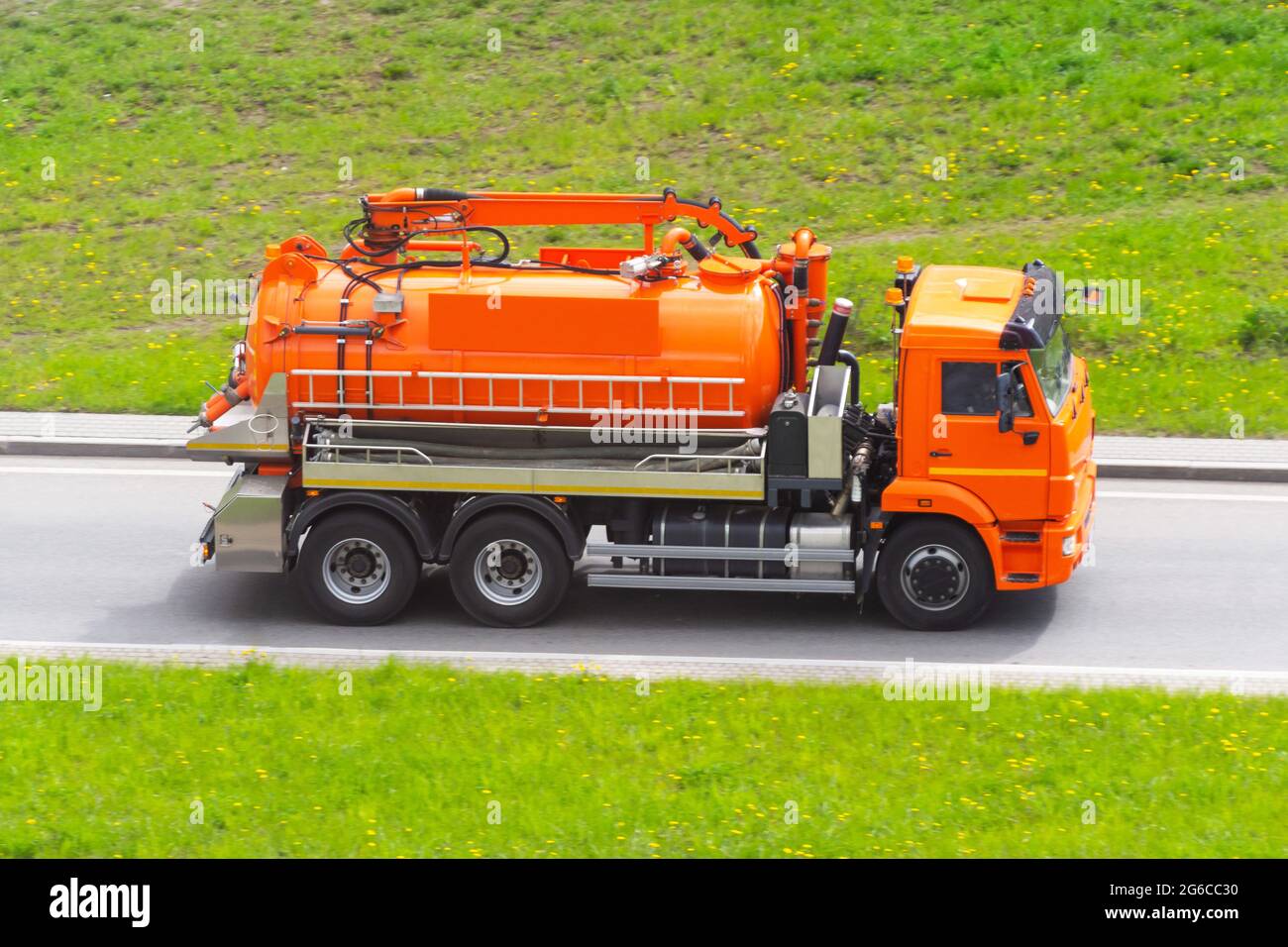 Il carrello arancione con un serbatoio e un sistema di pompaggio dell'acqua si muove in autostrada Foto Stock