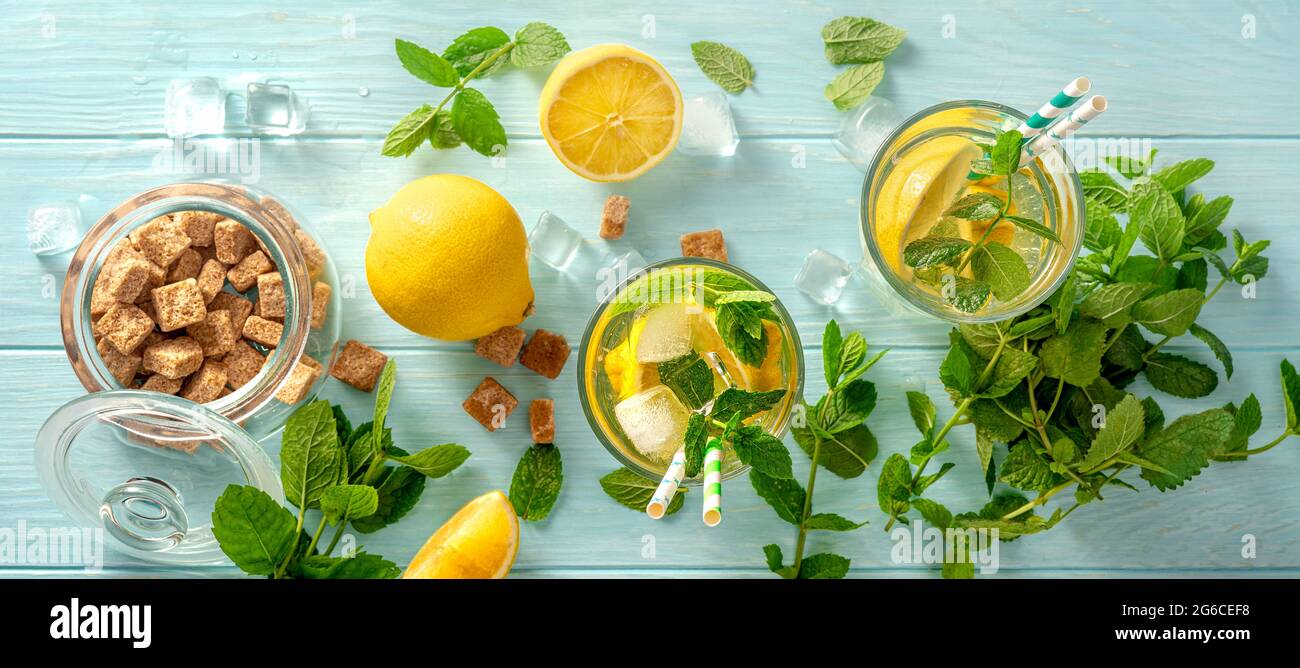 Bevande fredde estive in bicchieri con limoni, conchette su sfondo di legno blu. Vista dall'alto della limonata con zucchero di canna e cannucce di carta per bevande. Foto Stock