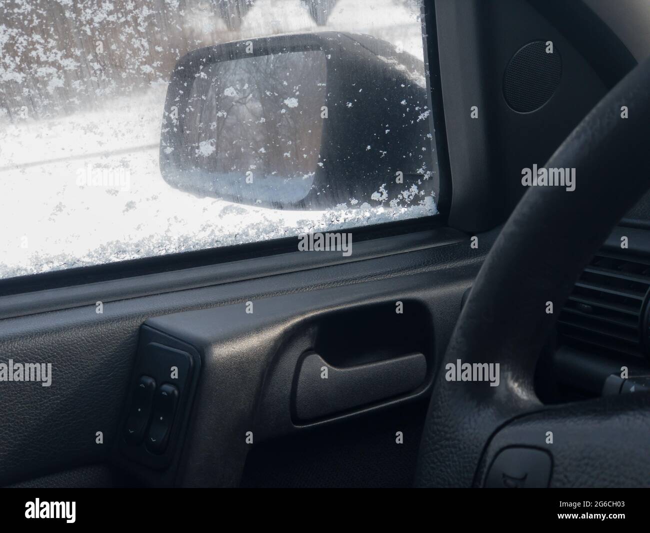 Vista sullo specchietto sinistro dall'interno del sedile di guida della vettura classica durante la stagione invernale della neve Foto Stock