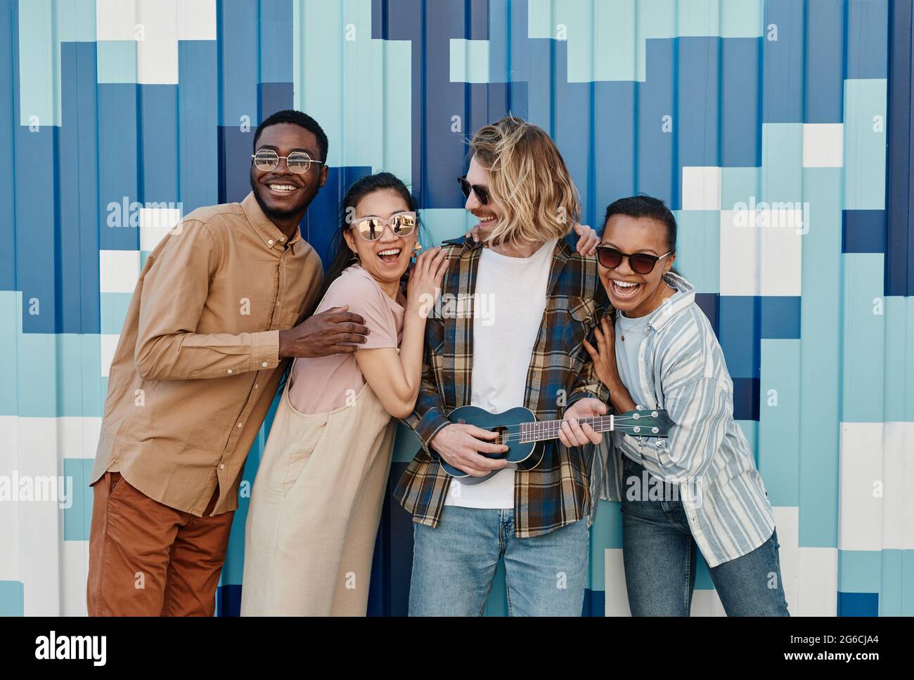 Gruppo vario di giovani che si posano all'aperto da un muro grafico in un ambiente urbano e sorridendo alla macchina fotografica Foto Stock