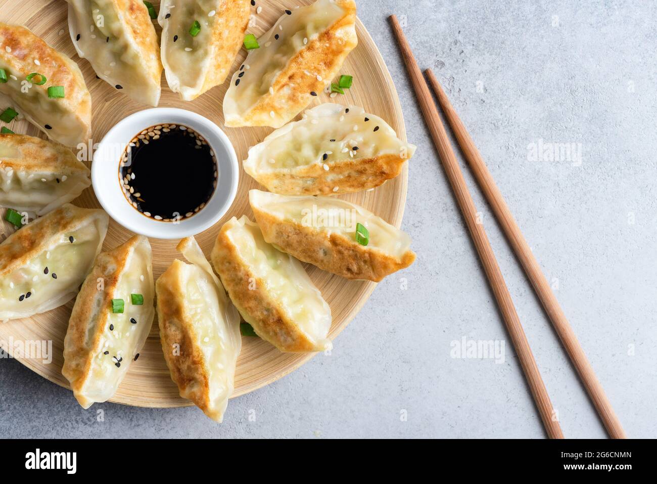 Gyoza o jiaozi, gnocchi cinesi fritti serviti con salsa di soia e semi di sesamo su piatto di bambù, vista dall'alto Foto Stock