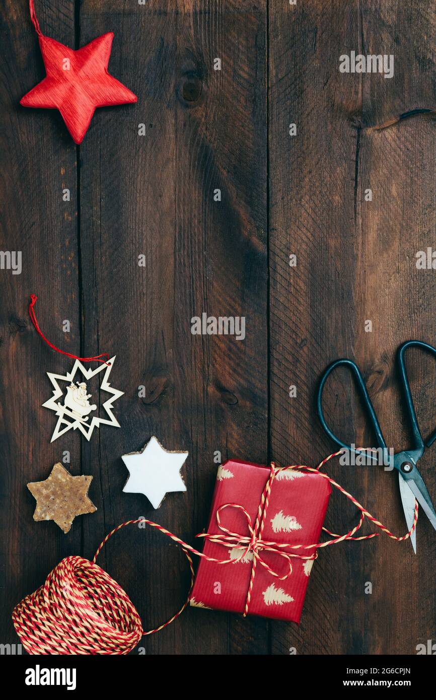 Scena regalo di Natale con presente, nastro, carta, biscotti e decorazione su rustico legno scuro, vista dall'alto con spazio copia Foto Stock