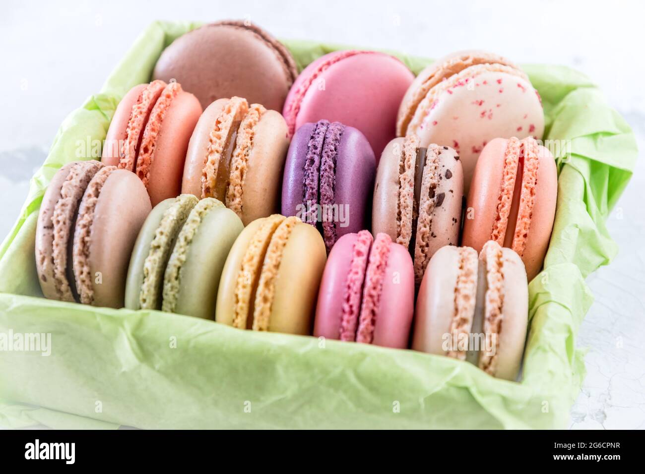 Macaron francesi colorati in una scatola verde su sfondo bianco Foto Stock