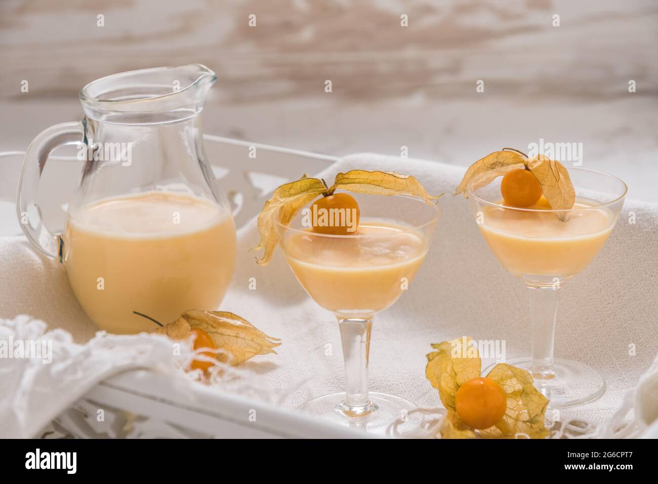 Due bicchieri e una caraffa con eggnog e frutti fisici su un vassoio di legno bianco su sfondo di marmo bianco Foto Stock