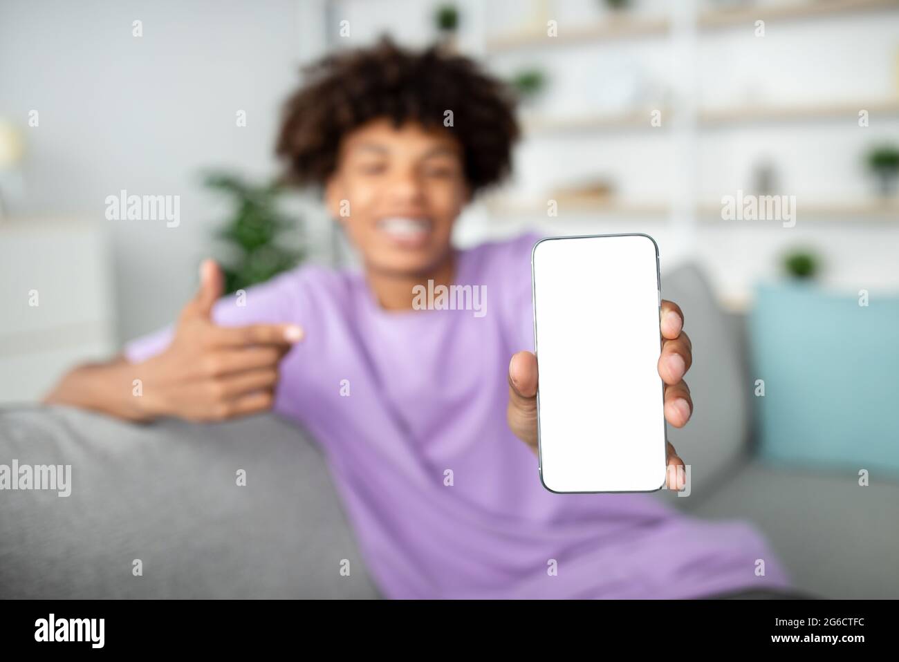 Positivo adolescente afroamericano che punta allo smartphone con mockup per app mobile sullo schermo, messa a fuoco selettiva Foto Stock