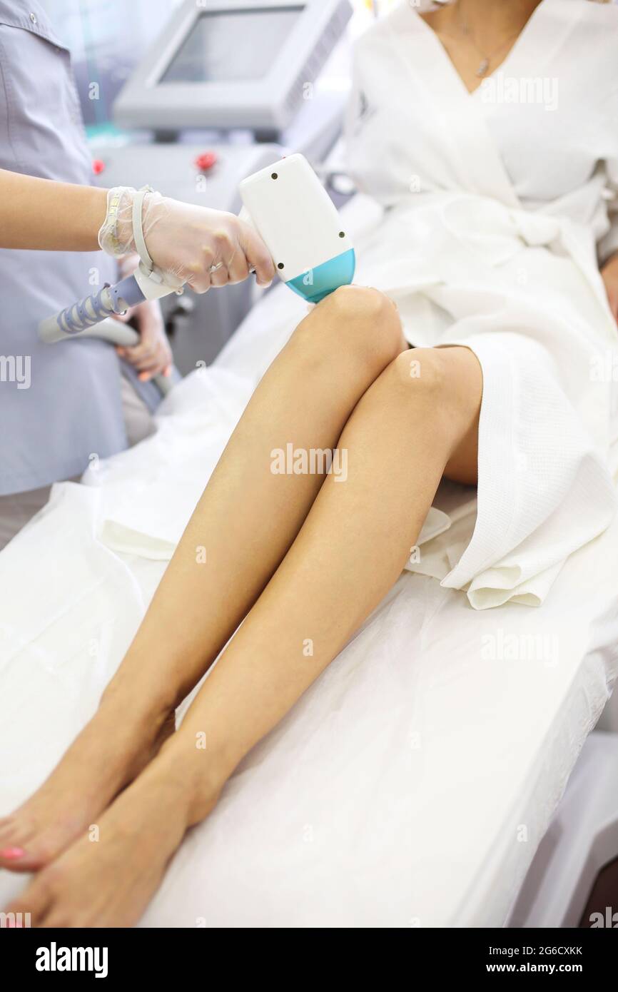 Dall'alto del cliente femminile che si trova sul divano nel salone di bellezza durante l'epilazione laser della gamba Foto Stock