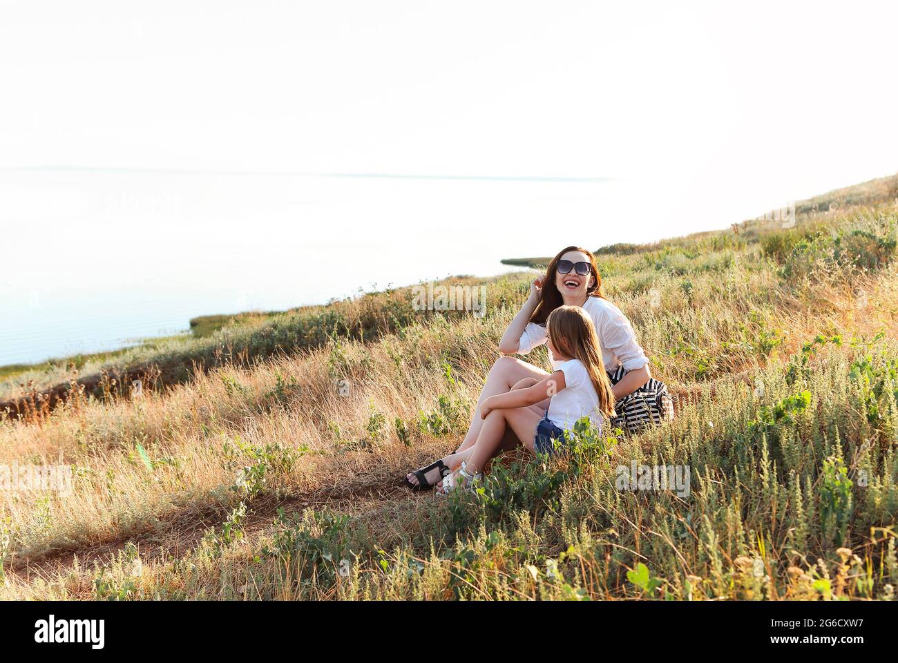 Sorridi madre e figlia coccolandosi dolcemente nel prato fiorente mentre trascorrete un fine settimana insieme in campagna e guardate la macchina fotografica Foto Stock