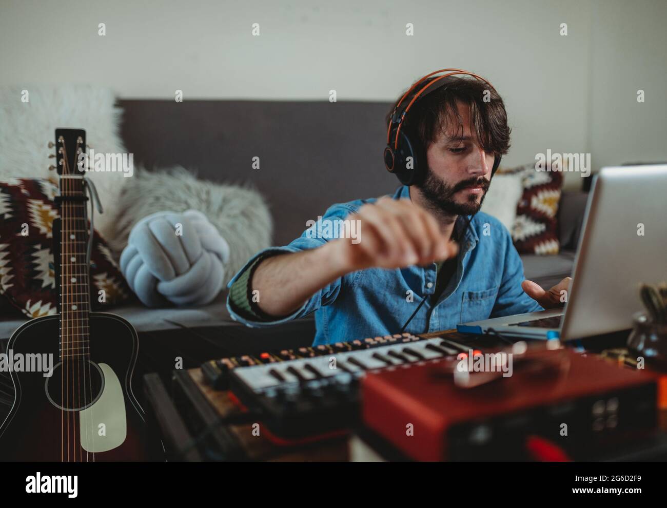 Giovane uomo in cuffia con sintetizzatore e computer portatile a casa Foto Stock