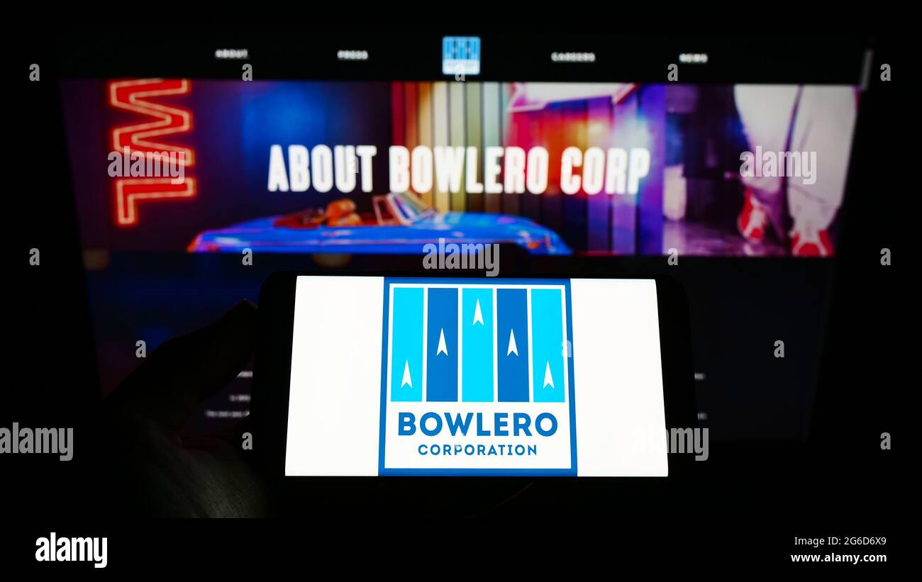 Persona che tiene il telefono mobile con il logo della società americana del centro di bowling Bowlero Corporation sullo schermo davanti alla pagina web. Mettere a fuoco il display del telefono. Foto Stock Persona che tiene il telefono mobile con il logo della società americana del centro di bowling Bowlero Corporation sullo schermo davanti alla pagina web. Mettere a fuoco il display del telefono. Foto Stock