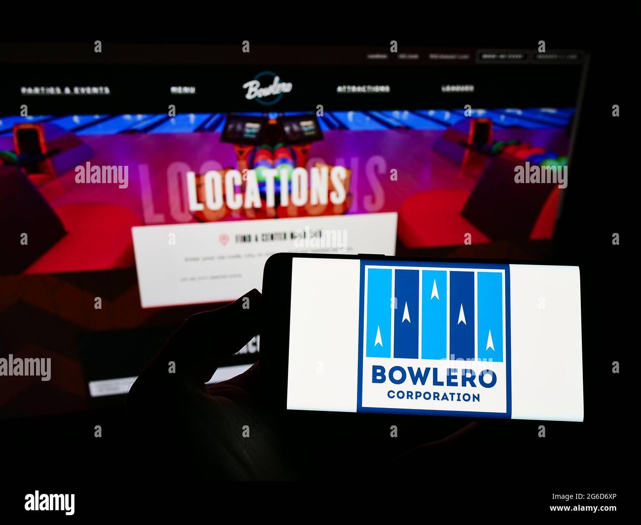 Persona che tiene il cellulare con il logo della società americana Bowlero Corporation del centro di bowling sullo schermo di fronte alla pagina web aziendale. Mettere a fuoco il display del telefono. Foto Stock Persona che tiene il cellulare con il logo della società americana Bowlero Corporation del centro di bowling sullo schermo di fronte alla pagina web aziendale. Mettere a fuoco il display del telefono. Foto Stock