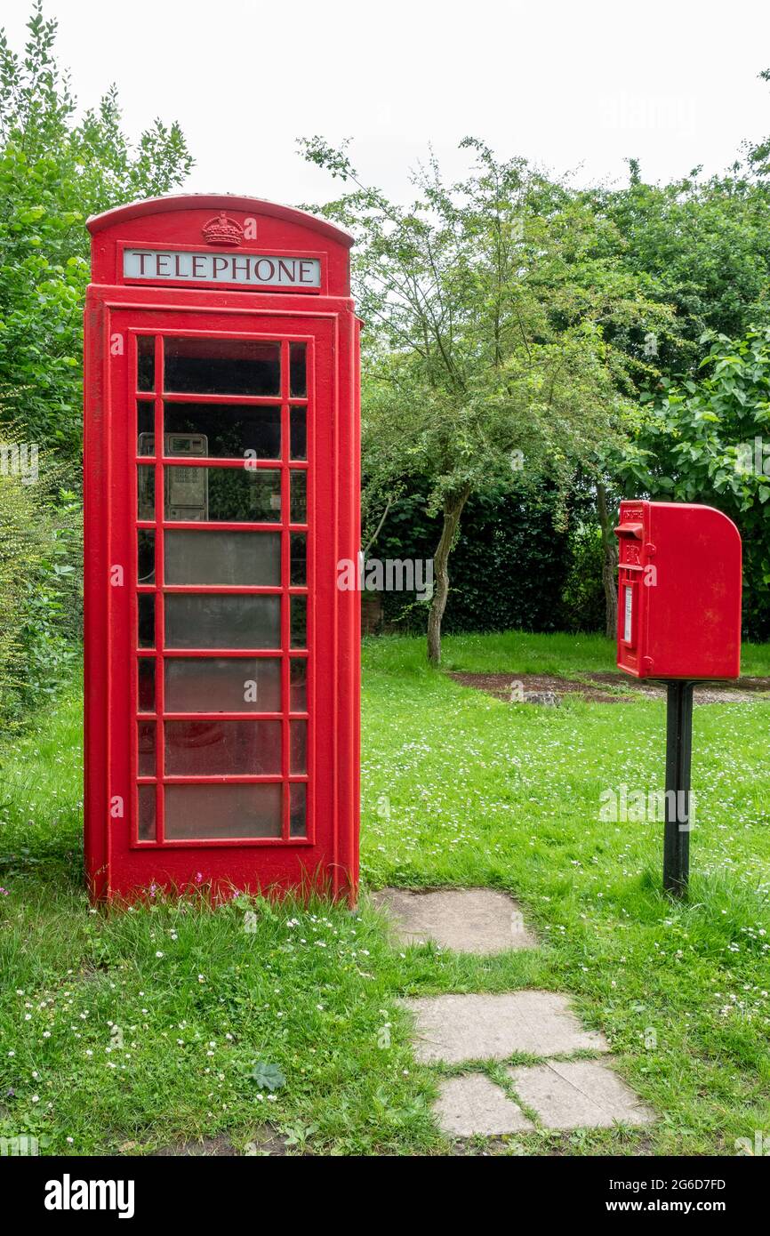 Una scatola telefonica rossa K6 e una scatola di distacco in ghisa montata su palo rosso in un ambiente rurale Foto Stock