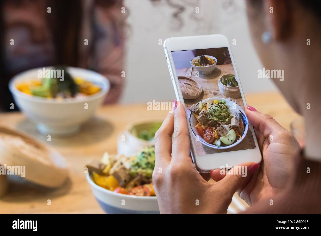 Donna irriconoscibile ritagliata scattando una foto del piatto di poke sullo smartphone mentre si passa il fine settimana in ristorante con un'amica femminile Foto Stock