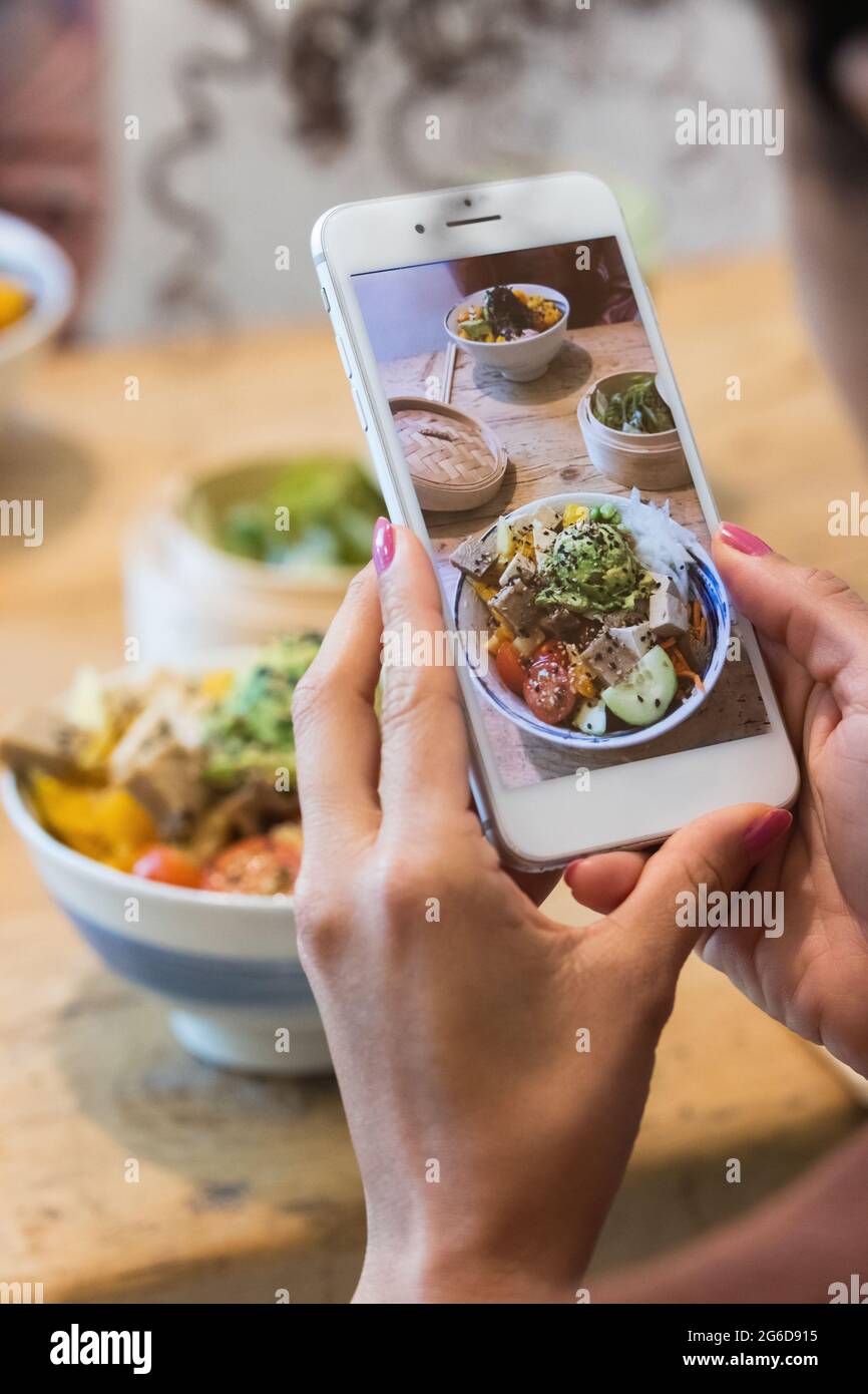 Donna irriconoscibile ritagliata scattando una foto del piatto di poke sullo smartphone mentre si passa il fine settimana in ristorante con un'amica femminile Foto Stock