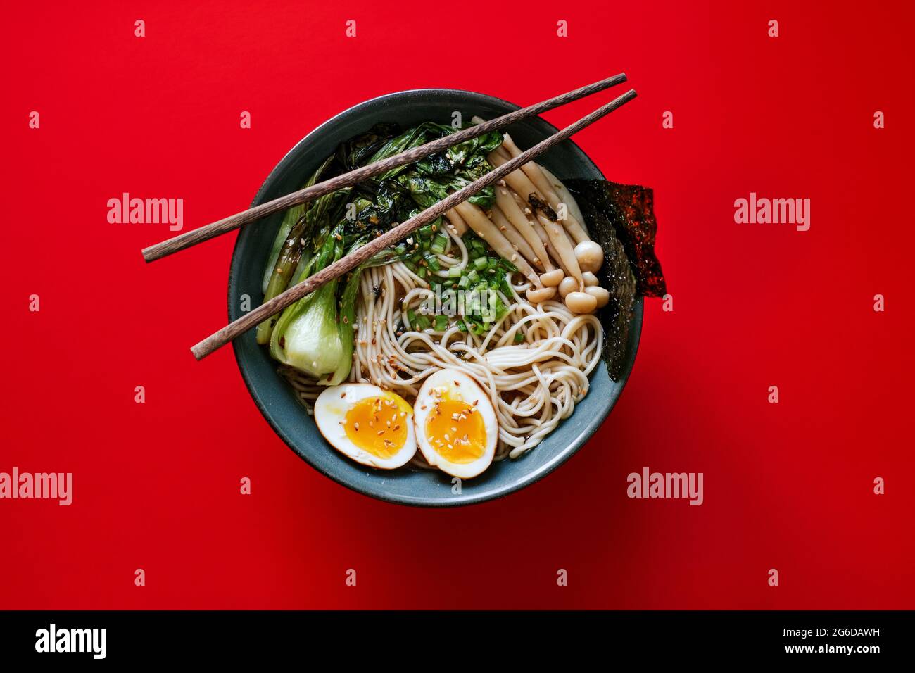 Vista dall'alto della ciotola in ceramica con deliziosi ramen e bastoncini posizionati su sfondo rosso Foto Stock